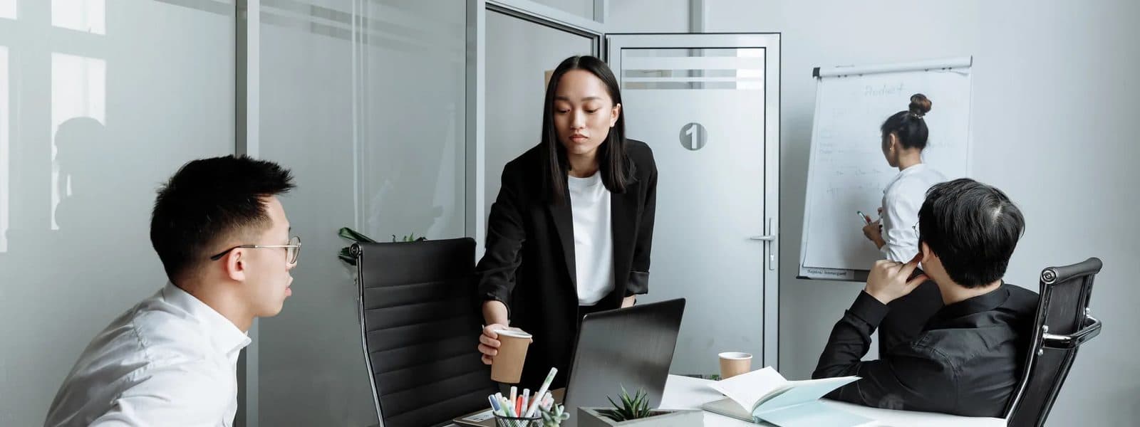 Colleagues in a meeting in a glass-walled office with a whiteboard behind them