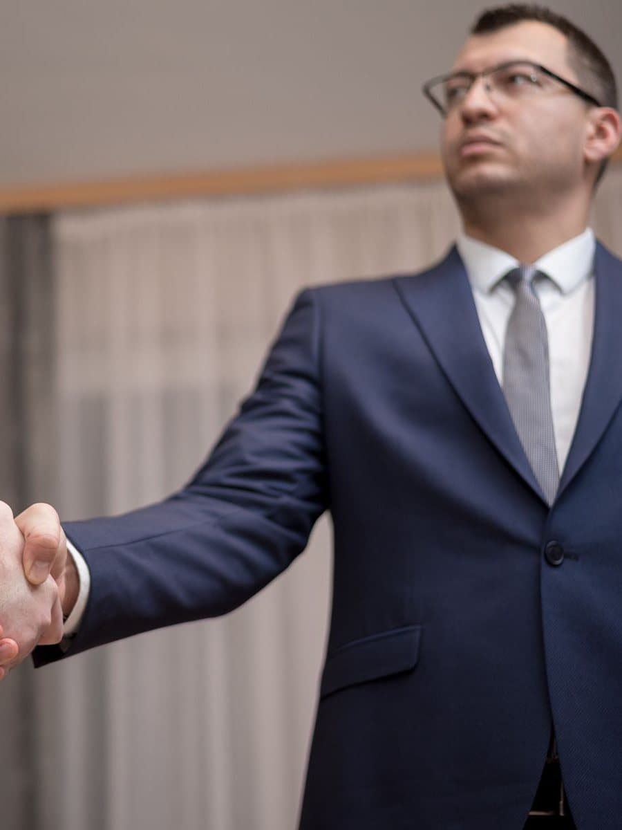 A businessman in a suit shaking hands with a supplier in an office