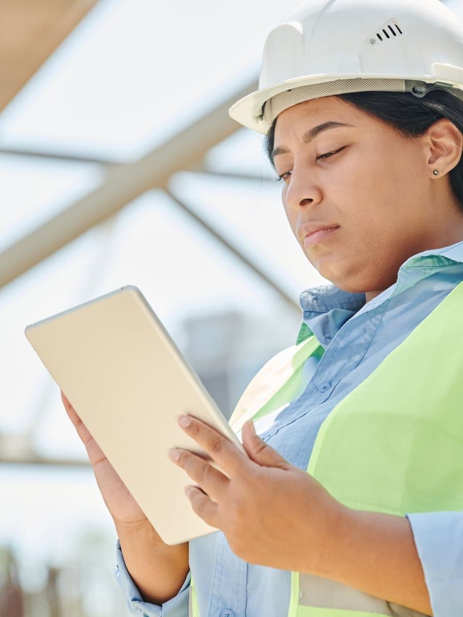 An engineer in a hard hat and safety vest reading a tablet on the shop floor