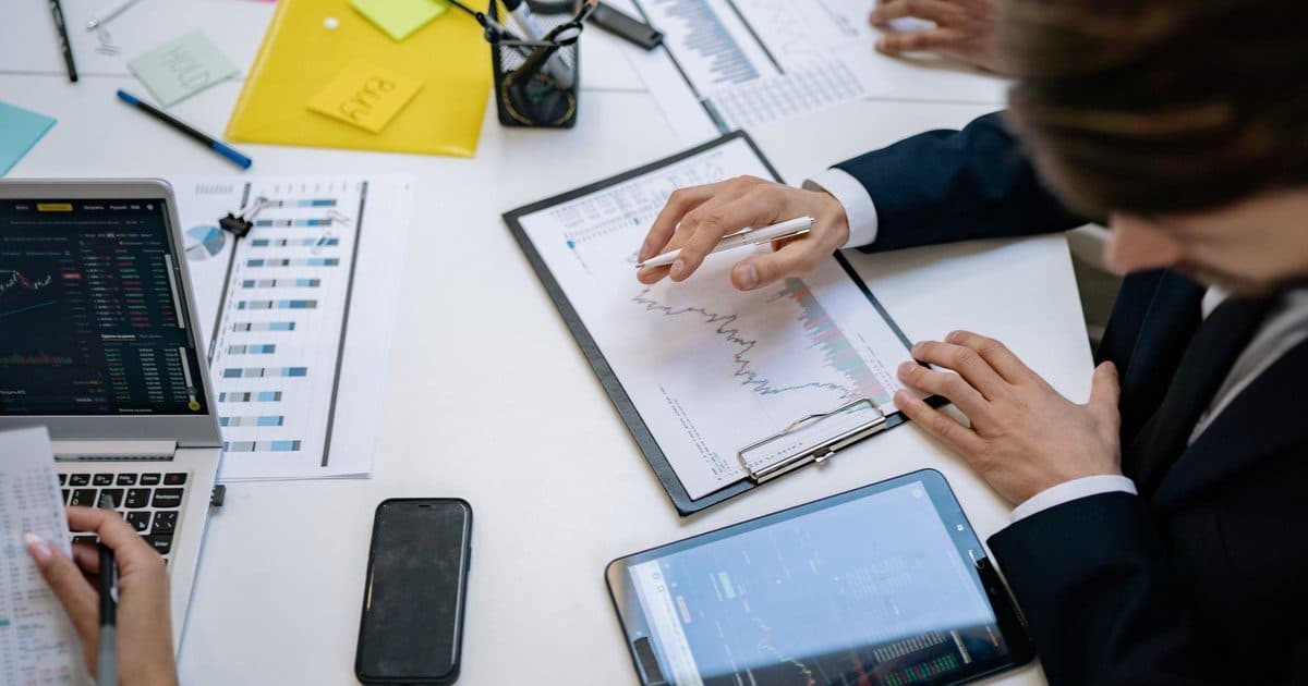 Analysts reviewing charts on a laptop, a tablet and printed reports