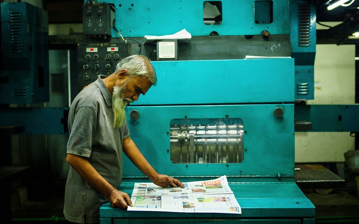A press operator checking a freshly printed sheet at a printing press